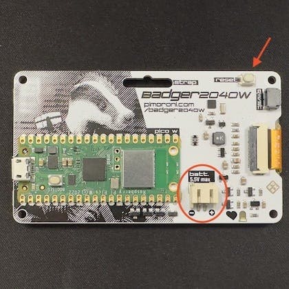 Back of the badge showing the reset button (arrow) and the connector for the batteries (circled)